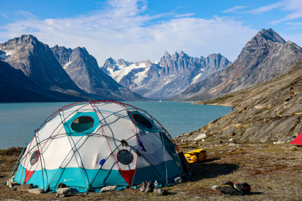 Campement en dôme au bord d’un fjord turquoise, entouré de montagnes escarpées au Groenland.